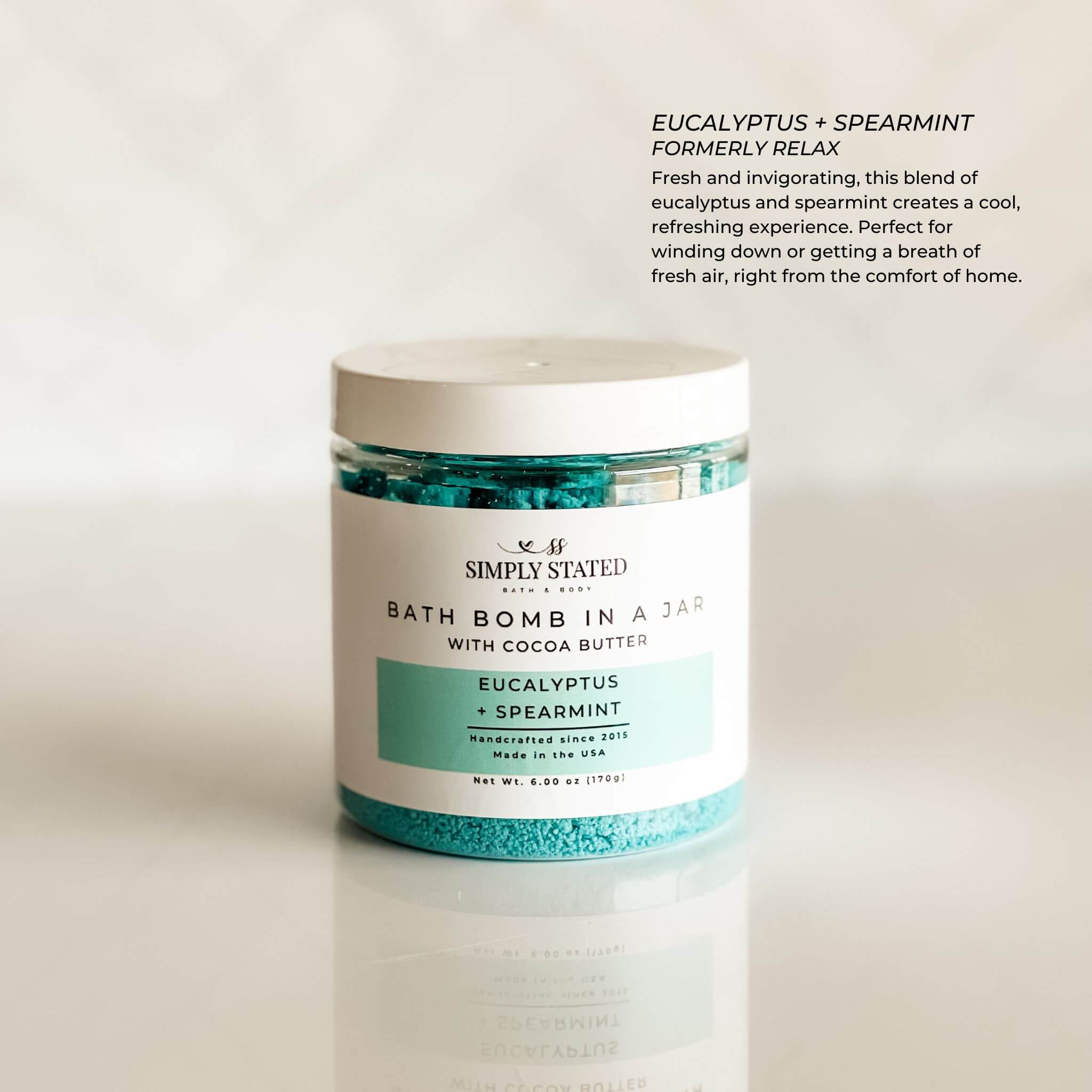 Aromatherapy bath bomb in a jar featuring the Eucalyptus + Spearmint blend. A refreshing mix of cool mint and invigorating eucalyptus for a spa-like self-care experience. Packaged in a clear jar with a minimalist label, highlighting its premium bath soak formula with cocoa butter for skin nourishment.