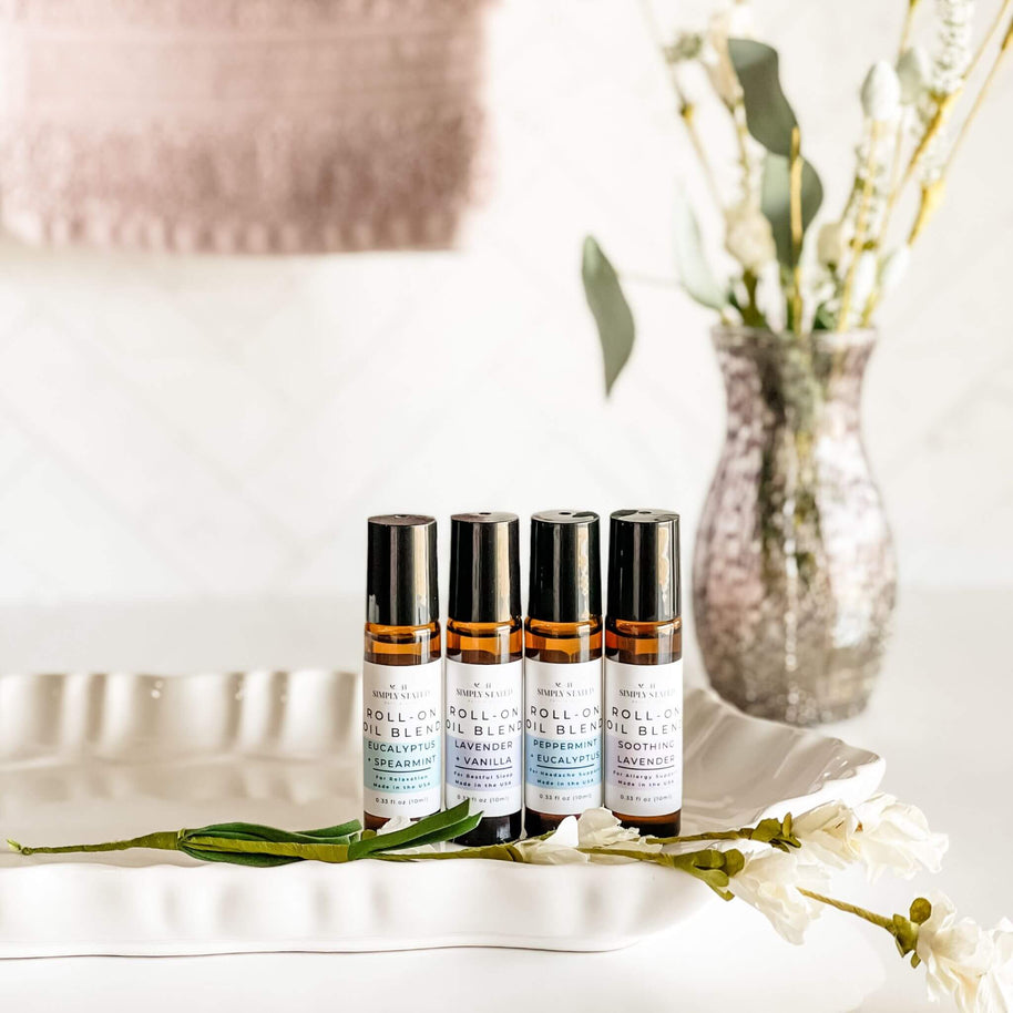 Four Simply Stated Bath & Body Roll-On Oil Blends, featuring Eucalyptus + Spearmint, Lavender + Vanilla, Peppermint + Eucalyptus, and Soothing Lavender. Arranged on a white tray with a calming floral aesthetic.