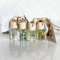 A set of car diffusers with clear glass jars and wooden lids, hanging from gold-colored chains.