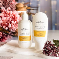 Two bottles of Simply Stated body cream on a decorative surface with flowers in the background