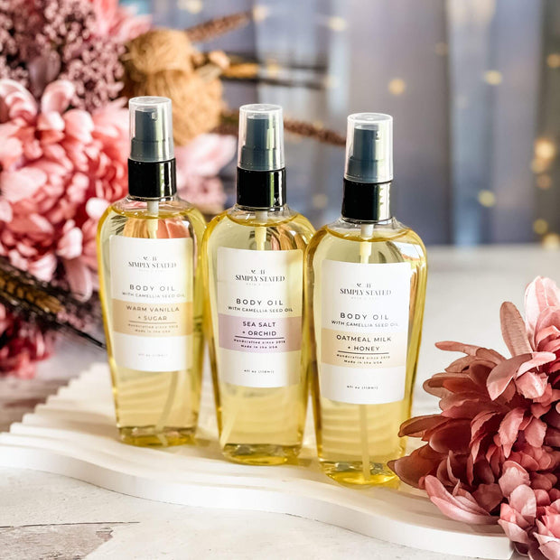 Three bottles of body oil with labels on a decorative surface with flowers.