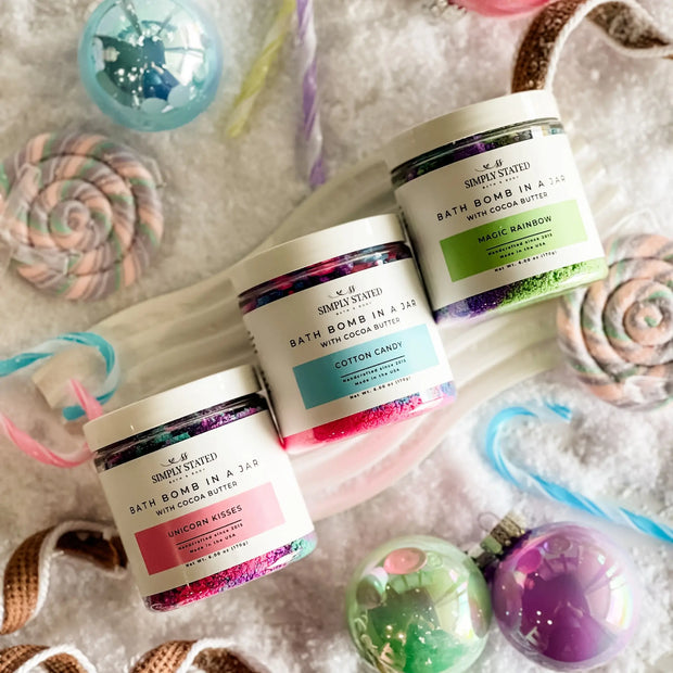 Three bath bomb containers with colorful labels on a textured surface with bath bombs and accessories.