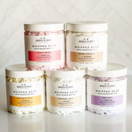 Collection of Signature Line Whipped Soaps in various scents, including Coconut Milk + Mango, Sweet Berry + Vanilla, Warm Vanilla + Sugar, Oatmeal Milk + Honey, and Sea Salt + Orchid, displayed in 8oz jars with whipped textures.