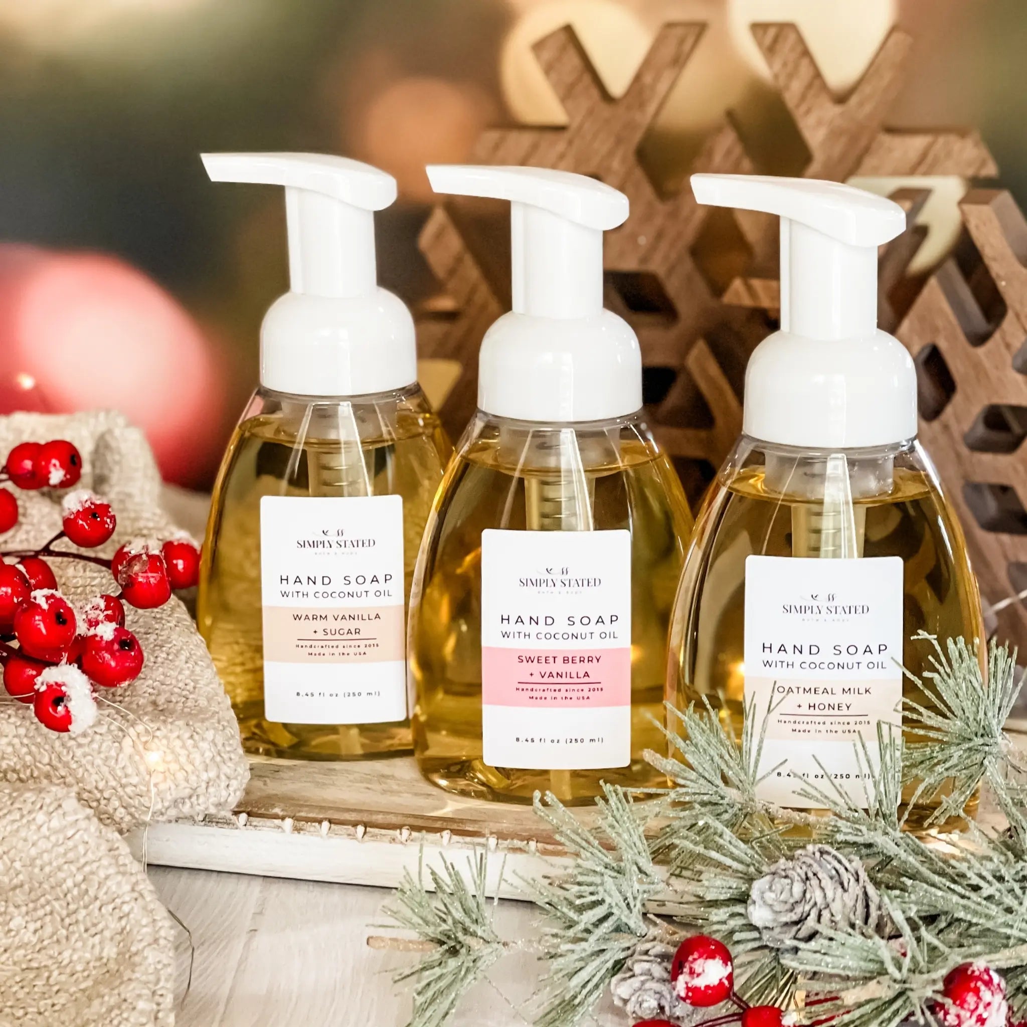 Three bottles of hand soap with pump dispensers on a decorative surface with Christmas elements.