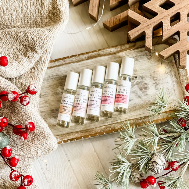 Five small perfume bottles on a wooden tray with Christmas decorations.