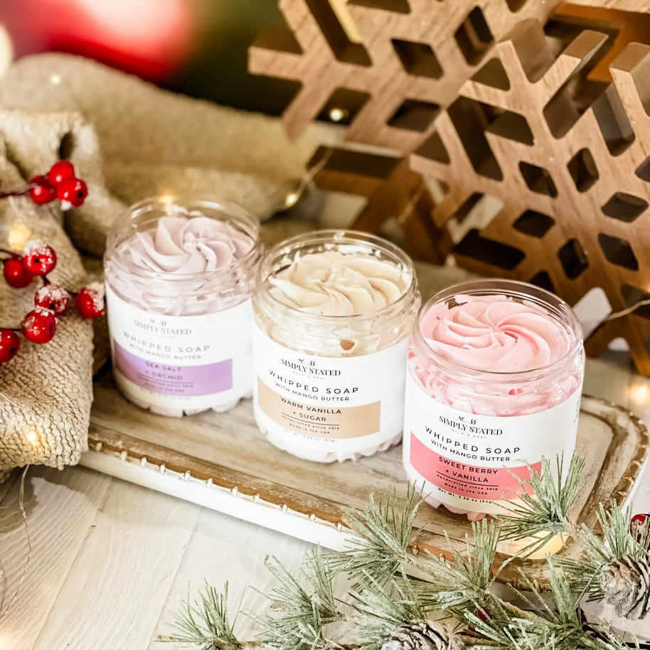 Three jars of whipped soap on a decorative tray with Christmas decorations.